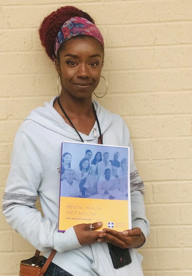 A woman holding up a book in front of a brick wall.